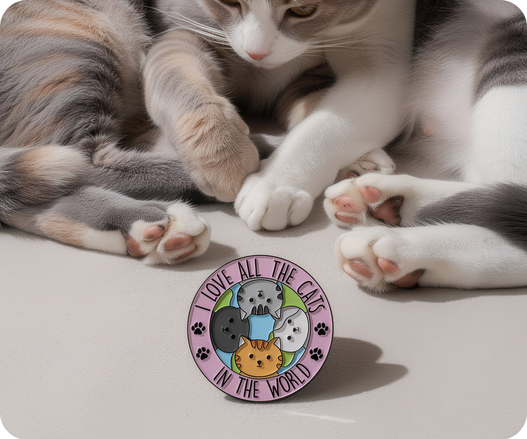Cat playing with a 'I love all the cats in the world' pin on a light surface. © Tigoli® 2026 All Rights Reserved Panda Loco Ltd 