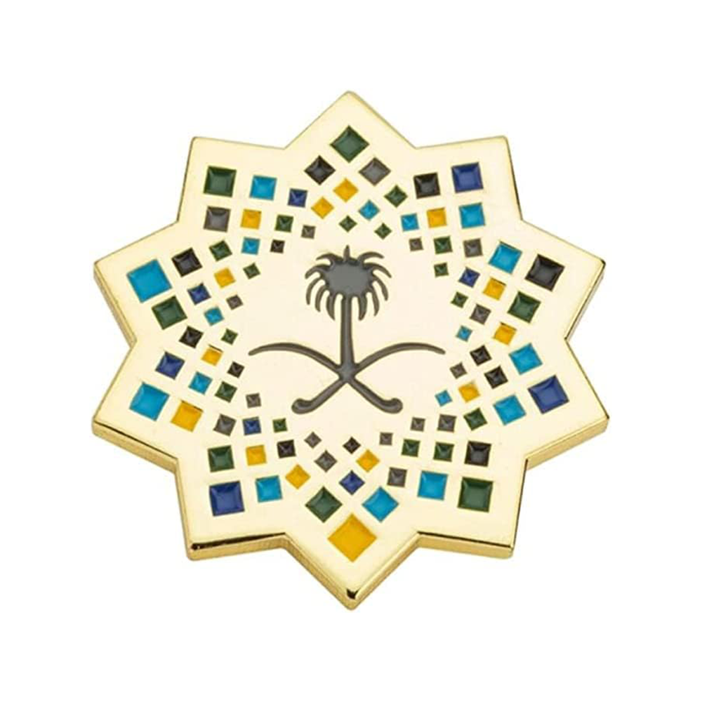 A pin badge shaped like a coconut tree with a star and the Saudi Arabia flag's colors.