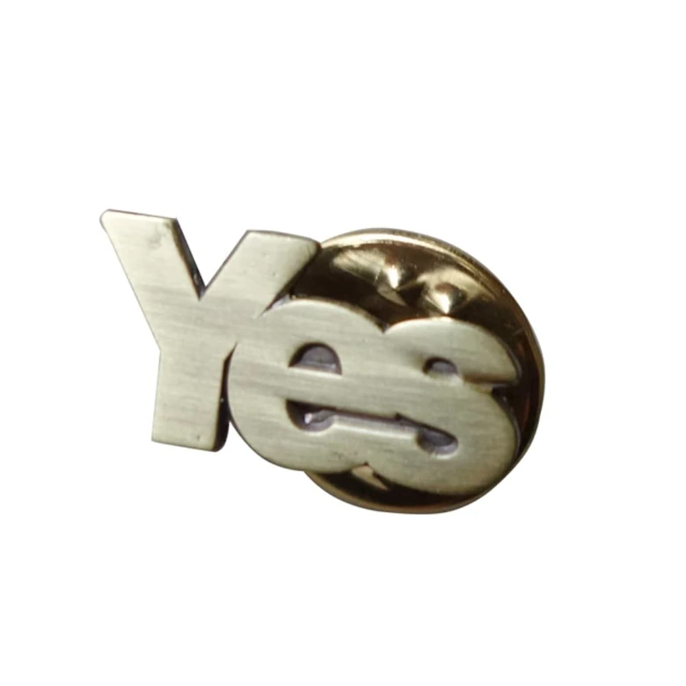 A brass pin badge with the word 'YES' in capital letters, designed for celebrating independence. © Tigoli® 2026 All Rights Reserved Panda Loco Ltd  Imagen principal del producto